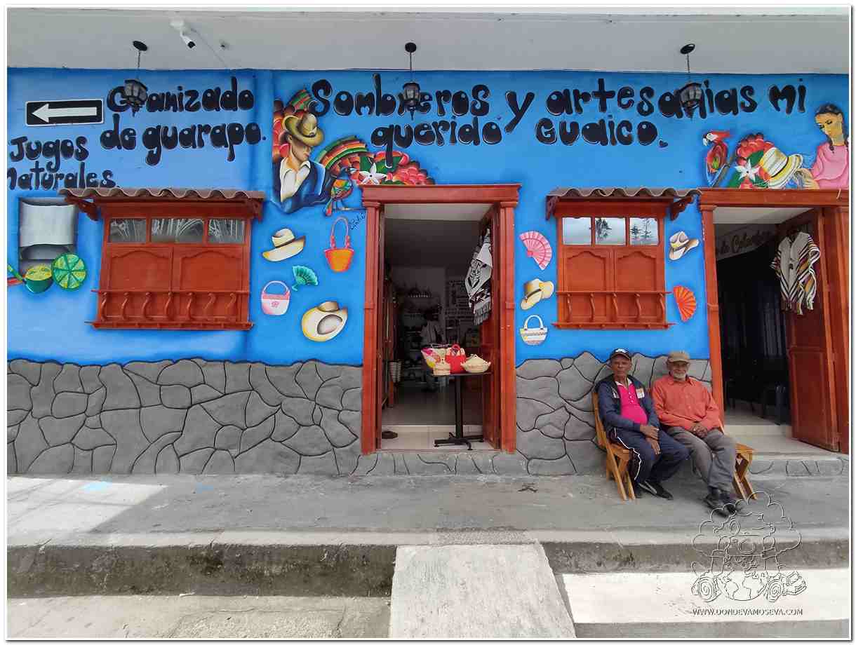 Fachada colorida de una tienda tradicional en Sandoná con vecinos conversando sentados al frente.