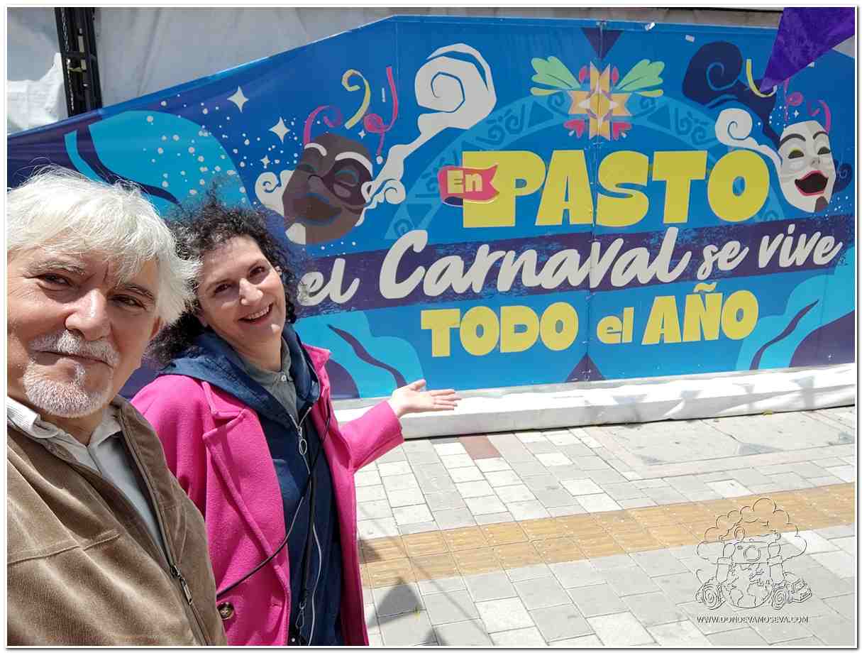 Pareja junto al cartel “En Pasto, el Carnaval se vive todo el año”, símbolo del espíritu permanente del Carnaval de Negros y Blancos.