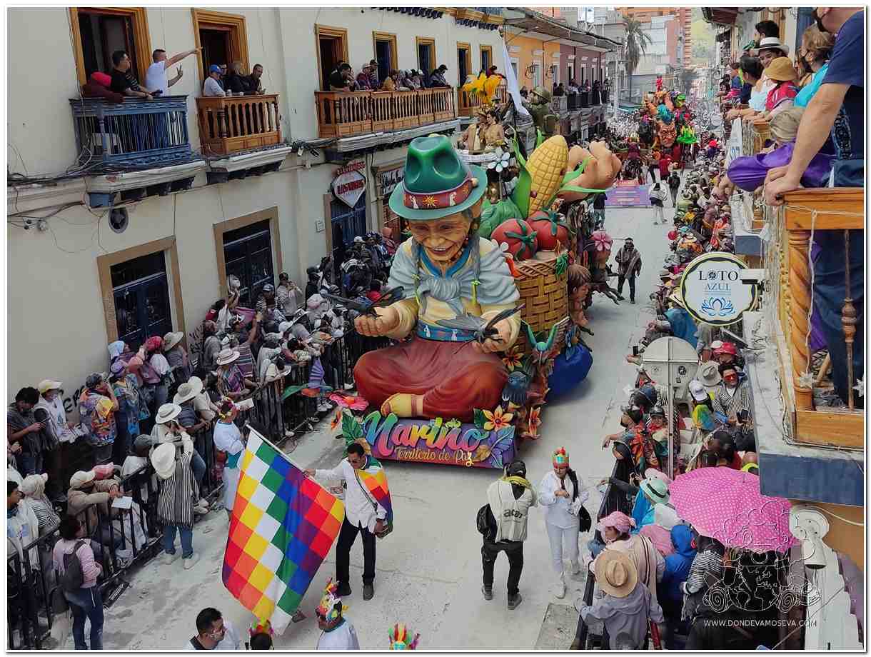 Carrozas monumentales desfilando por la Senda del Carnaval de Negros y Blancos de Pasto entre el público que celebra con espuma y música.