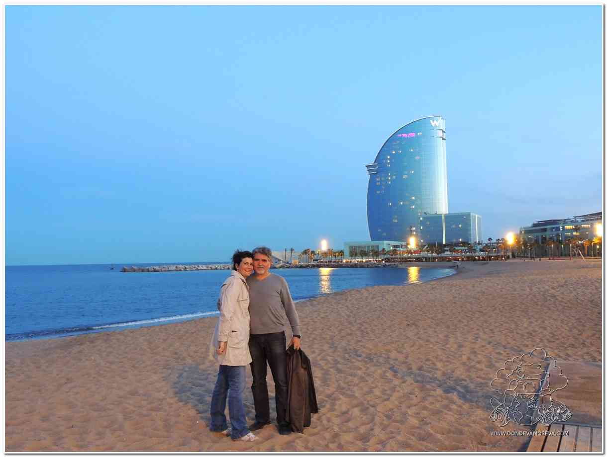 pareja disfrutando del mar de barcelona con el hotel vela al fondo